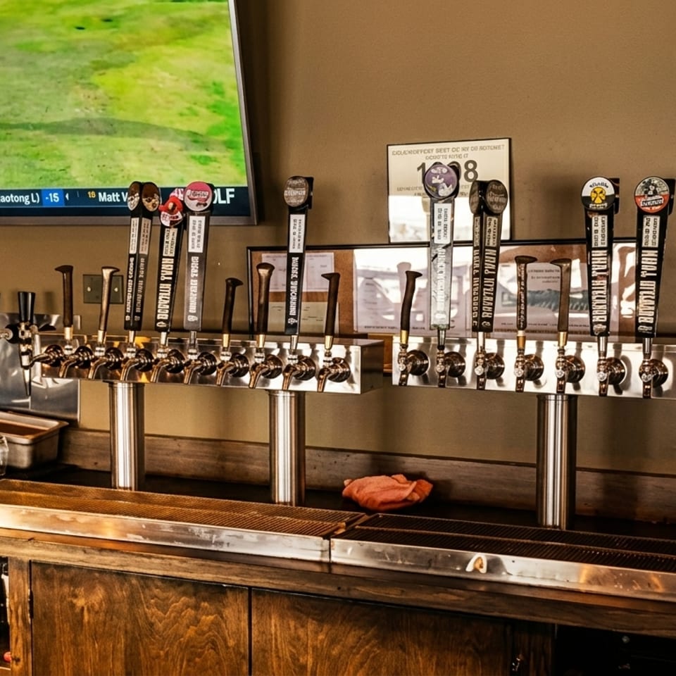 A bar counter with multiple beer taps, glasses, and a TV showing golf above.