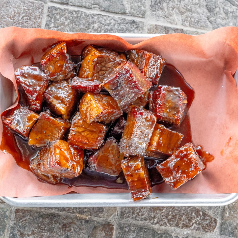 Tray of bite-sized glazed barbecue meat pieces served on parchment paper.