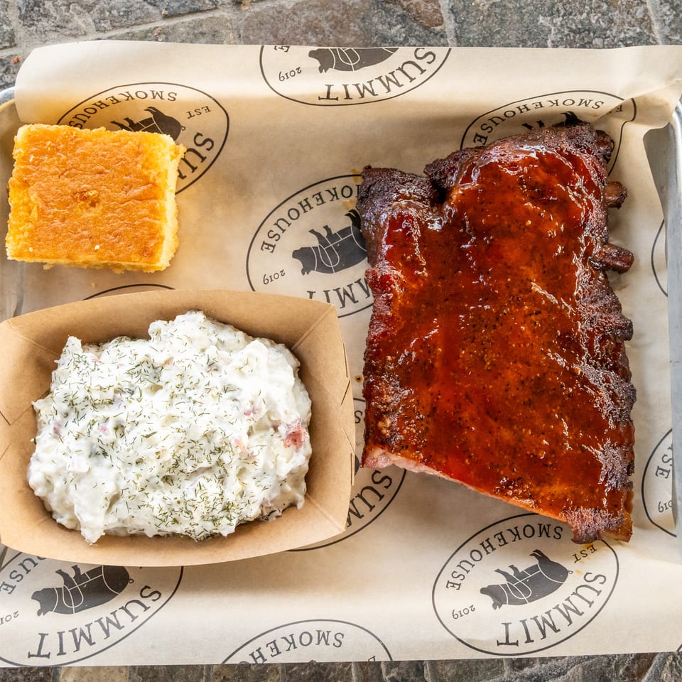 Tray of glazed barbecue ribs served with creamy dill potato salad and cornbread.