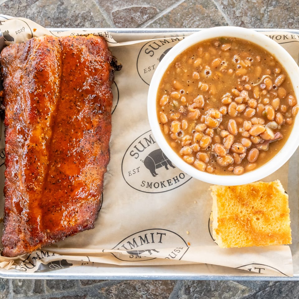 Barbecue tray with saucy smoked ribs, baked beans, and a square of golden cornbread.