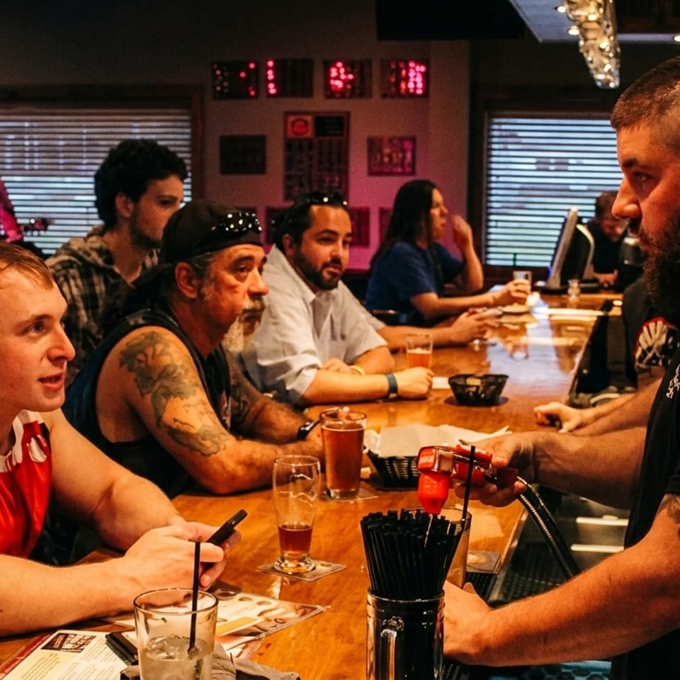 Bartender serving drinks to customers at a lively bar with a band playing in the background.